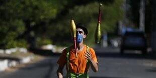 Ein Mann mit Mundschutz steht auf einer leeren Strasse undjJongliert