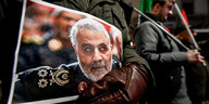 Ein Mensch in Militätuniform hält ein Foto des getöteten Generals Soleimani