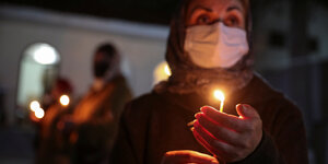 Eine Frau mit Mundschutz hält eine Kerze.
