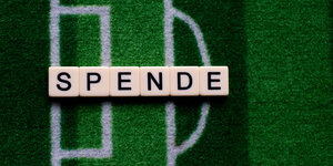 Auf einem Teppich, der wie ein Fußballfeld aussieht, ist mit Scrabble-Buchstaben das Wort "Spende" gelegt.