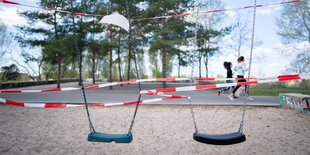 Zwei Schaukeln auf einem Spielplatz sind mit Flatterband abgeklebt