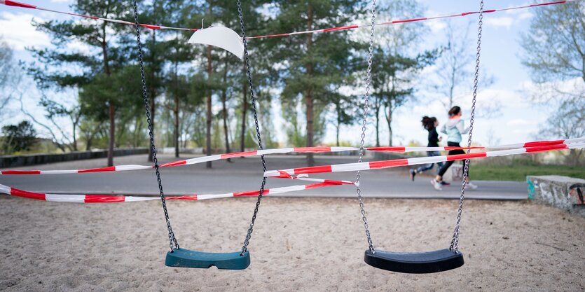 Zwei Schaukeln auf einem Spielplatz sind mit Flatterband abgeklebt