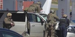 dpatopbilder - 19.04.2020, Kanada, Enfield: Polizisten bereiten sich darauf vor, an einer Tankstelle einen Verdächtigen in Gewahrsam zu nehmen.