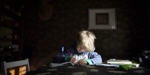ein Kind sitzt zu Hause und macht Hausaufgaben