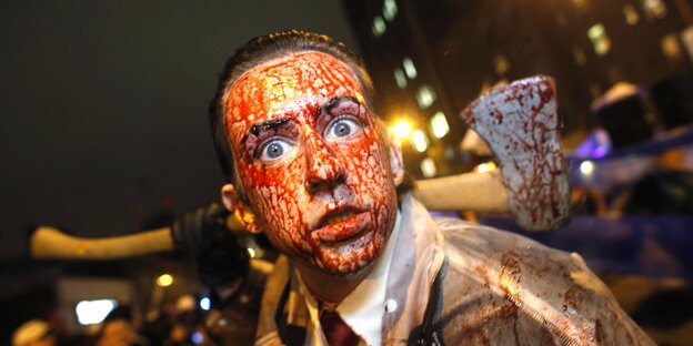 Ein Mann, blutverschmiert mit einer Axt in der Hand, guckt in die Kamera