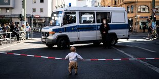 Ein kleines Kind vor einer Polizeiabsperrung.