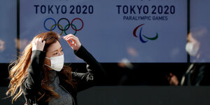 Eine Passantin mit Atemschutzmaske vor dem Logo der Olympischen Spiele