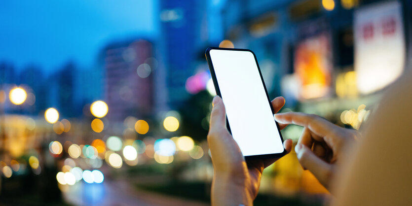 Blick auf ein beleuchtetes leeres Handy-Display, im Hintergrund eine unscharfe Straßenszene