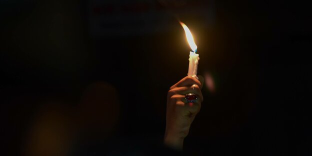 Eine Hand mit einer Kerze im Dunkeln.