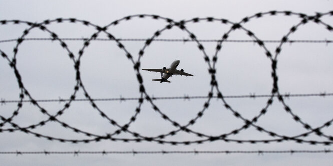 Ein Flugzeug steigt hinter einem Stacheldrahtzaun auf