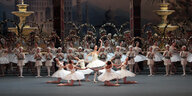 Eine sehr symmetrische Anordnung von Tänzerinnen in weißen Tutus vor großer Kulisse.