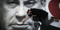 Eine Frau liegt auf einem großen Transparent mit dem Gesicht von Netanjahu.
