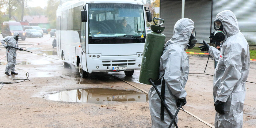 Personen in Schutzanzügen dekontaminieren einen Bus bei einer Strahlenschutz-Übung in Litauen.