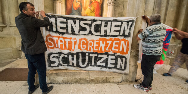 Flüchtlinge hängen im Dom St. Peter ein Transparent mit der Aufschrift "Menschen statt Grenzen schützen" auf.
