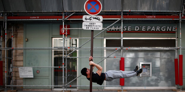 Ein Mann hängt sich quer an eine Verkehrschild, das vor einer Bank steht