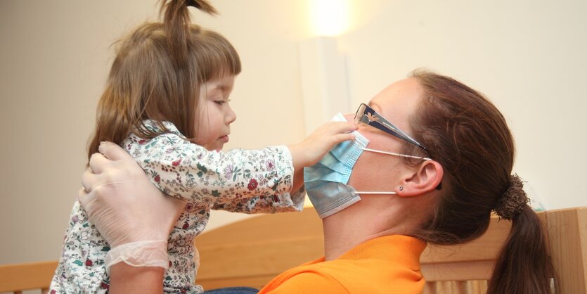 Eine Frau mit Mundschutz hebt ein Kind hoch.