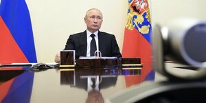 Valentin Putin sitzt an seinem Schreibtisch, im Hintergrund sind Fahnen zu sehen