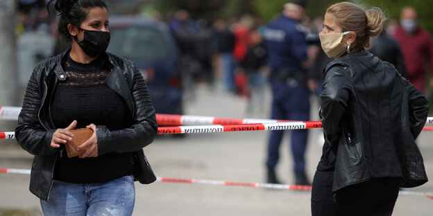 Zwei Frauen stehen an eine Absperrung aus weiß-rotem Polizeiband