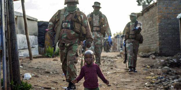 Soldaten gehen hinter einem kleinen Kind in einem Township.