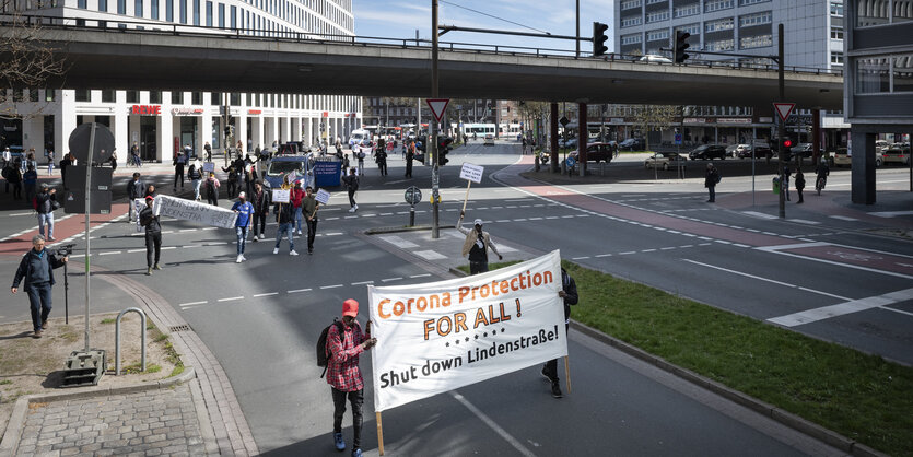 Zwei Männer auf einer Demo auf dem Weg vom Bahnhof in Höhe der Bremer Sozialbehörde tragen ein Schild, auf dem "Corona Protection for all" steht