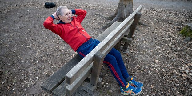 Ein älterer Mann macht Sportübungen auf einer Holzbank im Wald.