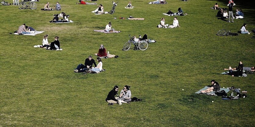 Sonnenhungrige halten Abstand auf einer Wiese in einem Berliner Park