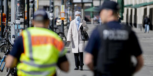 Zwei Polizisten und eine Frau mit Mundschutz auf einer Straße in Berlin in Corona-Zeiten