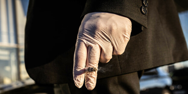 Eine Hand im Schutzhandschuh hält eine Zigarette.