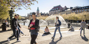 Mehrere Menschen an einem Stadtplatz mit Wasserfontäne.