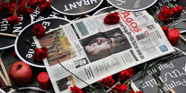 Dedenkveranstaltung für Hrant Dink. Eine Zeitung lieg auf dem Tisch. Um die Zeitung drapiert sind Rosen, Kerzen, Schilder und Granatäpfel.