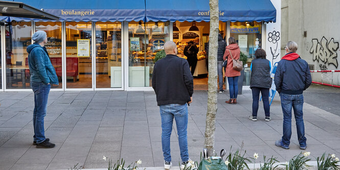 Leute stehen mit Abstand Schlange vor einer Konditorei