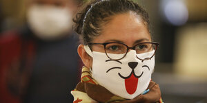Eine Frau mit einer Maske, auf die eine Katzenschnauze mit ausgestreckte Zunge aufgedruckt ist