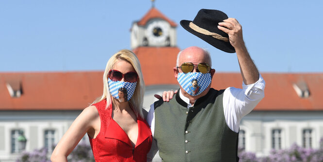 Zwei Menschen mit blau-weißen Trachtenmasken mit König Ludwig- und Sissy-Motiven