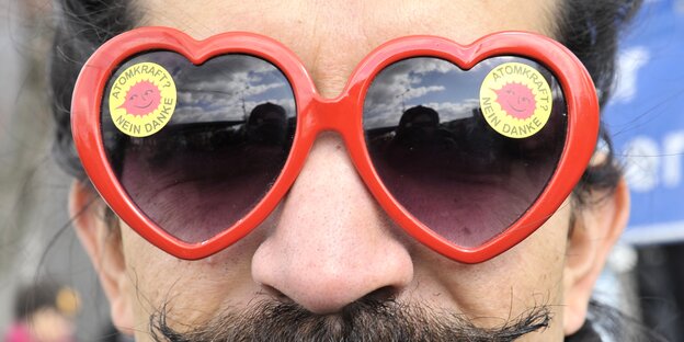 Ein Mann mit einer roten Sonnenbrille in Herzform, auf jedem Glas ein Atomkraft Nein Danke Aufkleber a in Herzform auf