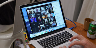 ein Laptop steht auf einem Tisch, auf dem Bildschirm eine Zoom-Konferenz