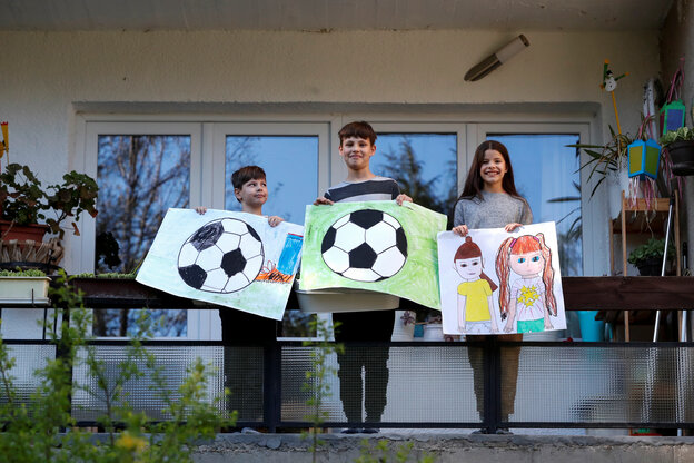 Drei Kinder mit selbstgemalten Bildern vor einem Haus