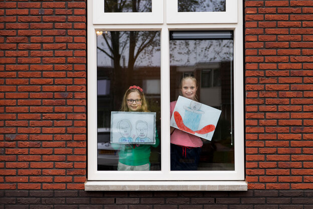 Zwei Kinder mit selbstgemalten Bildern hinter einer Fensterscheibe