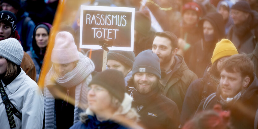 eine Demo, auf der ein Mensch ein Schild hochhält, auf dem steht: "Rassismus tötet"