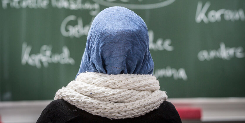 Eine Schülerin mit Kopftuch sitzt in einer Schule bei einer Unterrichtsstunde zum Thema Islam vor einer Tafel