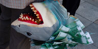Ein mensch hält eine Haifischpuppe mit Geldscheinen