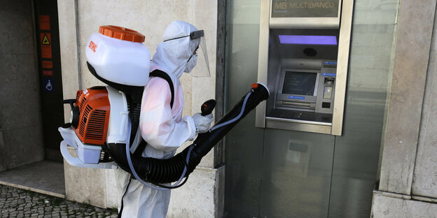 Eine Person in Schutzanzug desinfiziert einen Geldautomaten.