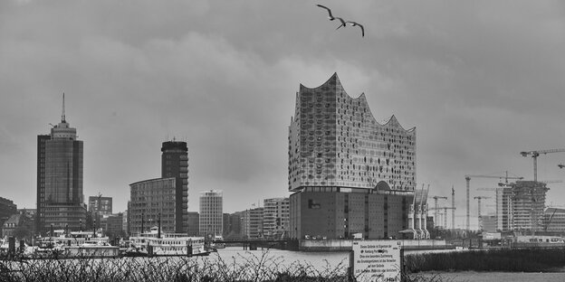 Über der Hafencity von Hamburg hängen Regenwolken. Hinter der Elbe ist die Silhouette der Hafencity zu sehen. Besonders groß: die Elbphilharmonie.