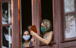 Zwei Frauen mit Mundschutz am Fenster, eine richtet das Handy in Richtung Straße