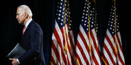 Joe Biden geht aus dem Bild, man sieht US-Amerikanische Flaggen.