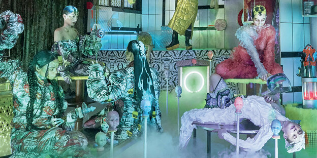Fünf alienhafte Wesen sitzen und liegen auf Gegenständen vor einem bunten psychedelischen Hintergrund