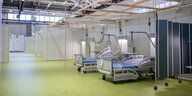 Leere Krankenhausbetten und Trennwände stehen in einer großen Halle mit Blechdach