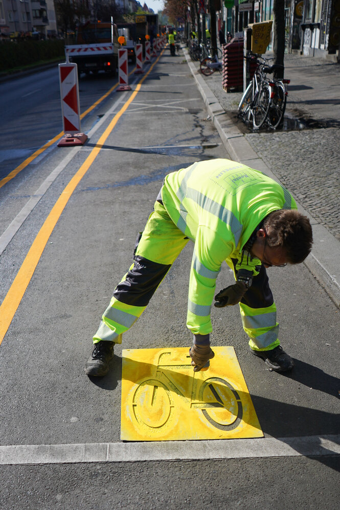 Ein Arbeiter in Schutzkleidung sprüht ein Fahrradsymbol auf einen temporären Radstreifen