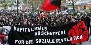 Eine Demo mit vielen schwarz gekleideten Menschen mit einem Banner gegen den Kapitalismus