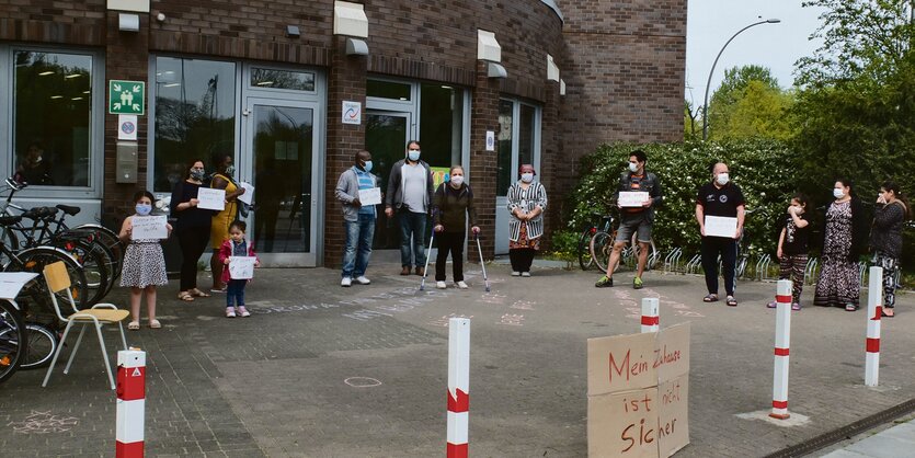 Menschen mit Mundschutz demonstrieren vor einem Backsteingebäude