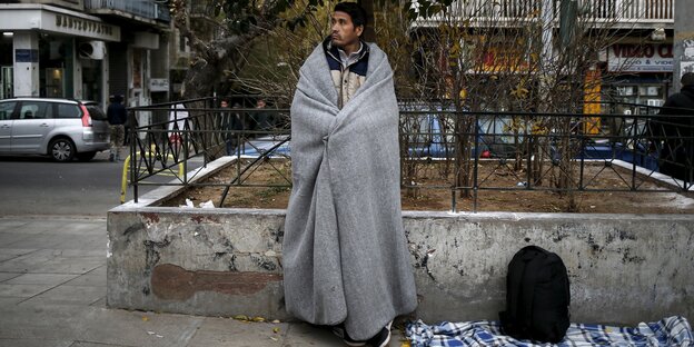 Ein afghanischer Migrant steht mit einer Decke um die Schultern gewickelt auf dem Viktoria-Platz in Athen, einem Aufenthaltsort von Geflüchteten